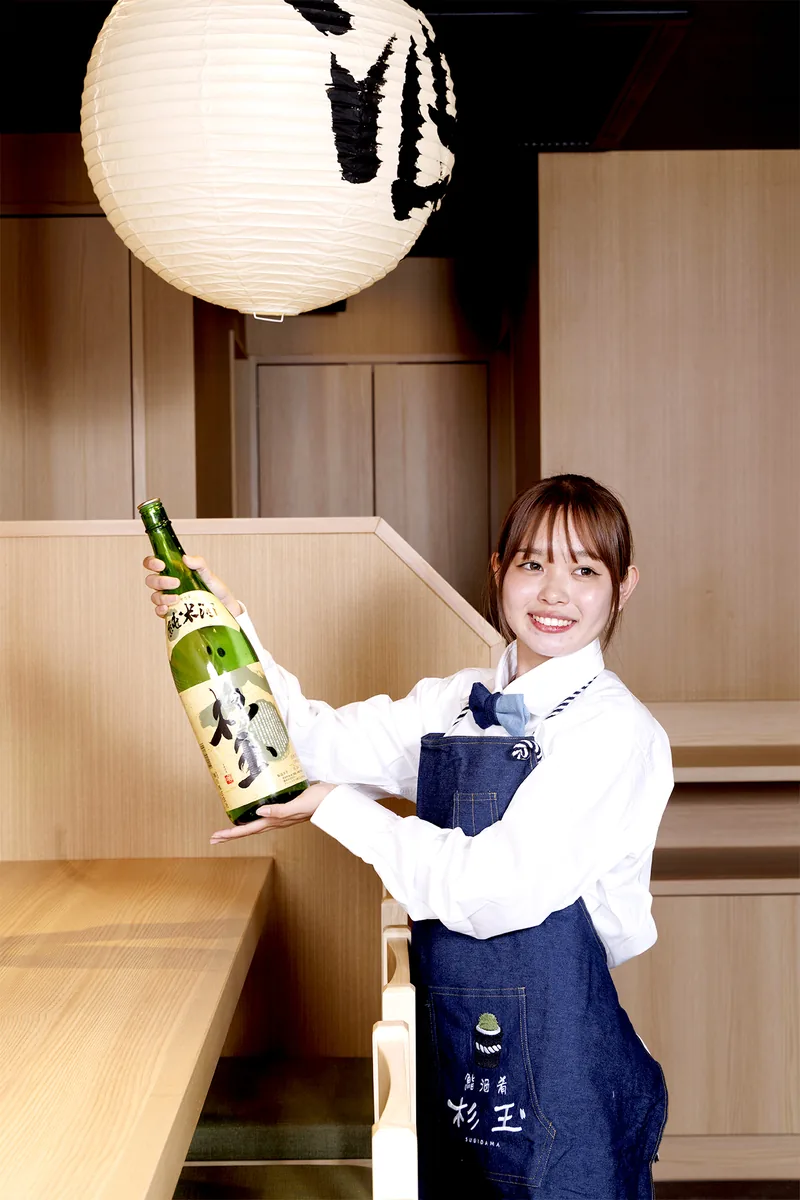 日本酒の瓶を手にしたスタッフと提灯の下がる店内
