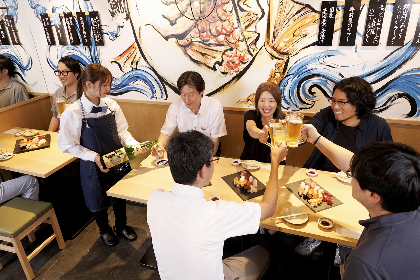 壁画のある店内のテーブル席で料理とお酒を囲むお客様